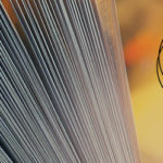 A closeup of an open book with fanned pages, on a warm, amber-colored backdrop, featuring the logo for Oleb Books.