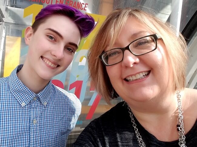 Mom and son, 18-year-old, purple-haired Sebastian and Stephanie Duesing smile at the camera together.