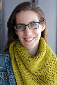 Author Laura Perna, wearing a bright, knit scarf and glasses, smiles at the camera.